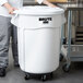 A man in a chef's uniform holding a large white Rubbermaid ingredient storage bin.