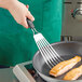 An OXO fish turner being used to cook salmon in a pan.