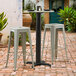 A Lancaster Table & Seating black outdoor table base with bar stools on a brick patio.