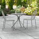 A Lancaster Table & Seating Harbor Gray outdoor patio table with two chairs on a patio.