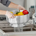 A person in gloves washing peppers in a Choice aluminum colander.