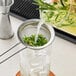 A person pouring liquid through a Choice stainless steel fine mesh strainer with herbs.
