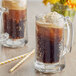 A glass mug of root beer with a straw next to a bottle of J. Hungerford Smith Root Beer Concentrate.