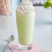 A glass of milkshake with green J. Hungerford Smith Creme De Menthe syrup, whipped cream, and a spoon.