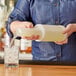 A person pouring liquid from a white Choice pour bottle into a glass with ice.