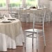 A Lancaster Table & Seating silver resin Chiavari chair next to a table with white linens.