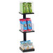 A black Cal-Mil 3-tier metal display stand holding green and clear packages of snacks.