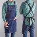 A man wearing a denim Outset BBQ apron with pockets.
