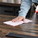 A hand wiping a table with a red WypAll foodservice wiper.