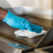 A hand wearing blue gloves cleaning a school kitchen counter with a white WypAll X50 foodservice wiper.