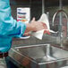 A man cleaning his hands at a sink in a professional kitchen with Kleenex Premiere paper towel.