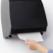 A hand pulling a paper towel from a black paper towel dispenser.