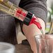A person using a TableCraft red spout liquor pourer to pour liquid into a glass.
