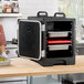 A black front-loading insulated food pan carrier with a red hot board and multiple trays inside.