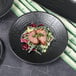 A close-up of an Elite Global Solutions matte black melamine plate with salad and meat on it.