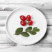 An Elite Global Solutions white melamine plate with cherry tomatoes and a leaf on it.