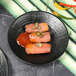 Two Elite Global Solutions matte black embossed melamine plates with salmon and peppers on them.