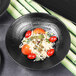 A black matte melamine bowl filled with pasta, tomatoes, and greens.