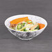 A black marble embossed melamine bowl filled with vegetables and noodles on a table.