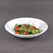 An Elite Global Solutions black marble embossed melamine bowl filled with salad with tomatoes and greens.