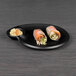 A black Elite Global Solutions melamine plate with food and dipping sauce.