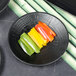 A close up of a Denali matte black melamine plate with sliced peppers on it.