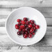 A white Elite Global Solutions melamine bowl filled with cranberries on a wooden table.