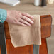 A hand using a Quickie brown microfiber cloth to dust a wooden chair.