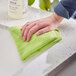 A hand wiping a kitchen counter with a green Quickie microfiber cloth.