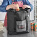 A woman putting a can of soda into a black Choice insulated tote bag.