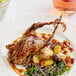 A white plate topped with a Manchester Farms fresh whole quail and vegetables on a table with a glass of wine.