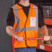 A man in an Ergodyne orange high visibility vest with an ID holder holding a red handle.