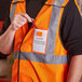 A person wearing an orange Ergodyne high visibility vest with an ID holder holding a pen.