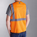 An Ergodyne orange mesh safety vest with reflective stripes being worn by a person.