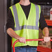 A man wearing a Ergodyne lime green high visibility safety vest holding a red handle.