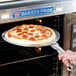A person using an American Metalcraft pizza pan gripper to remove a pizza from an oven.