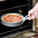 A person using an American Metalcraft cast aluminum pizza pan gripper to remove a pizza from an oven.