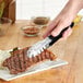 A person using Choice stainless steel scalloped tongs to cut a steak.