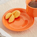 An Acopa Valencia Orange stoneware saucer with a cup of tea on it.