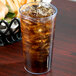 A Cambro clear plastic tumbler filled with ice tea on a table with a sandwich in the background.