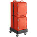 A red CaterGator food pan carrier with a strap on a black cart with orange plastic containers inside.
