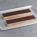 Rectangular white toque opera strip cakes covered in chocolate on a white tray.