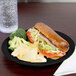 A Cambro black polycarbonate narrow rim plate with a sandwich and chips.