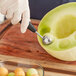 A hand using an OXO melon baller to scoop a melon.