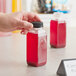 A hand holding an 8 oz. tall square PET clear juice bottle filled with red liquid.