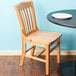 A Lancaster Table & Seating natural finish wood school house chair next to a table.