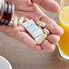 A hand holding a Multisorb StripPax desiccant packet next to a bowl of pills on a table.