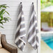Two Monarch Brands Aston & Arden gray and navy striped pool towels hanging on a wall.