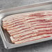 A tray of Warrington Farm Meats smoked sliced bacon on a gray surface.
