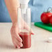 A hand pouring red sauce into a Cylinder PET Sauce Bottle.